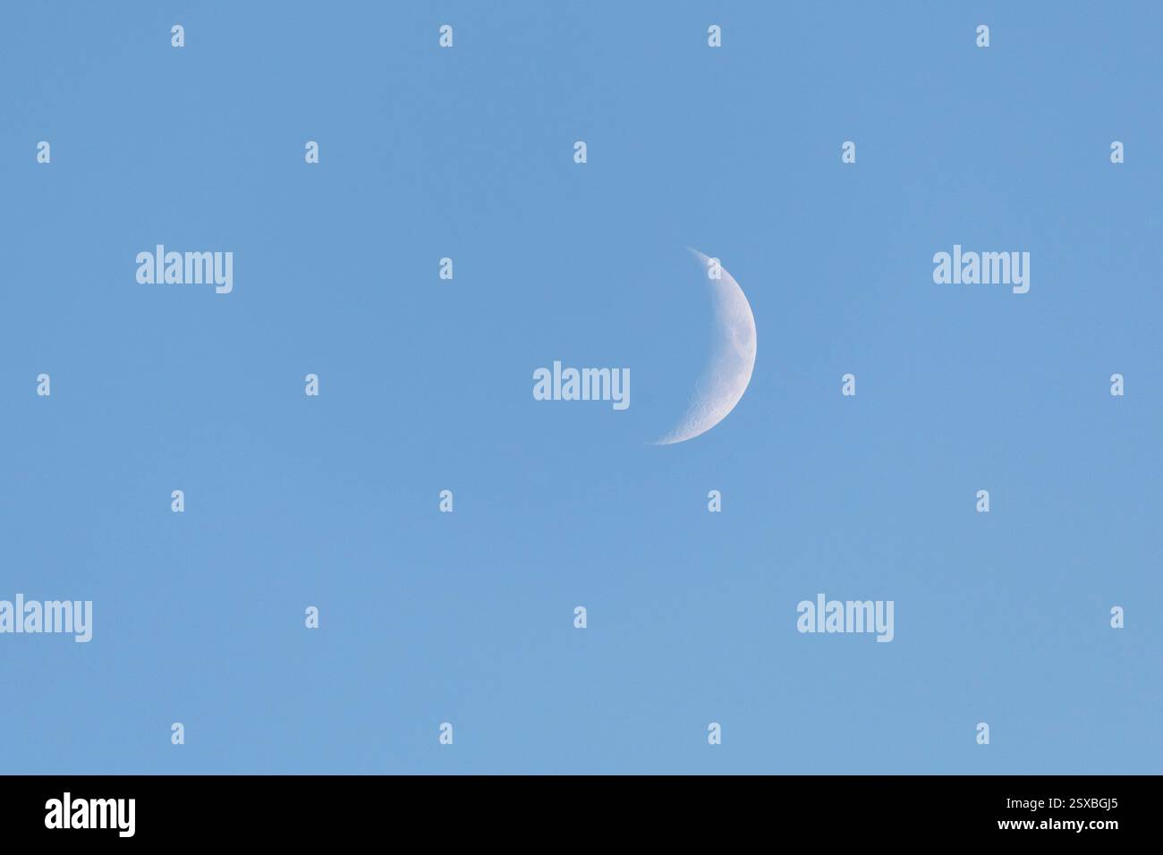 Der Mond in der wachsenden Halbmondphase des Mondzyklus, sichtbar in einem klaren, blauen Himmel am späten Winternachmittag. Stockfoto