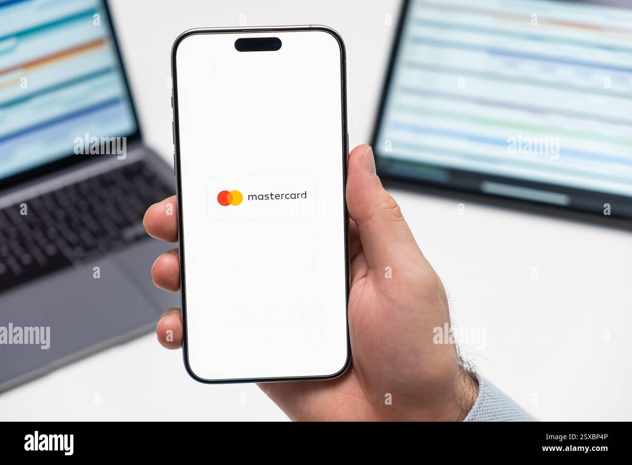 PRAG, TSCHECHISCHE REPUBLIK - 21. JANUAR 2024: Mastercard-Logo auf dem Bildschirm des Smartphones in der Hand des Mannes auf dem Hintergrund des Arbeitsplatzes. Stockfoto