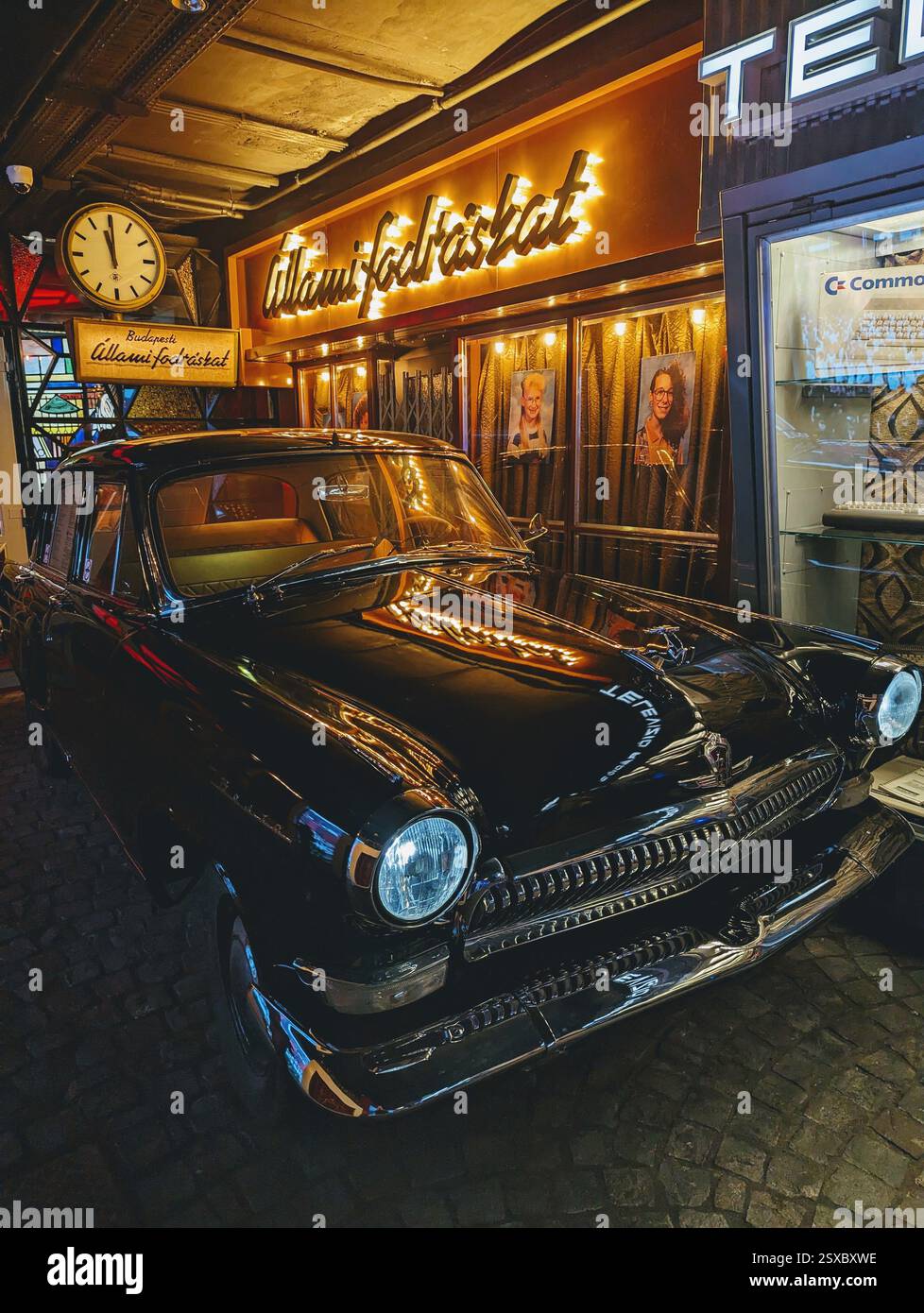 Ein wunderschön erhaltener schwarzer Oldtimer leuchtet unter Neonlichtern im Retro Museum Budapest und fängt die nostalgische Essenz der ungarischen Vergangenheit ein. - Smartphone-aufgenommenes Stockfoto