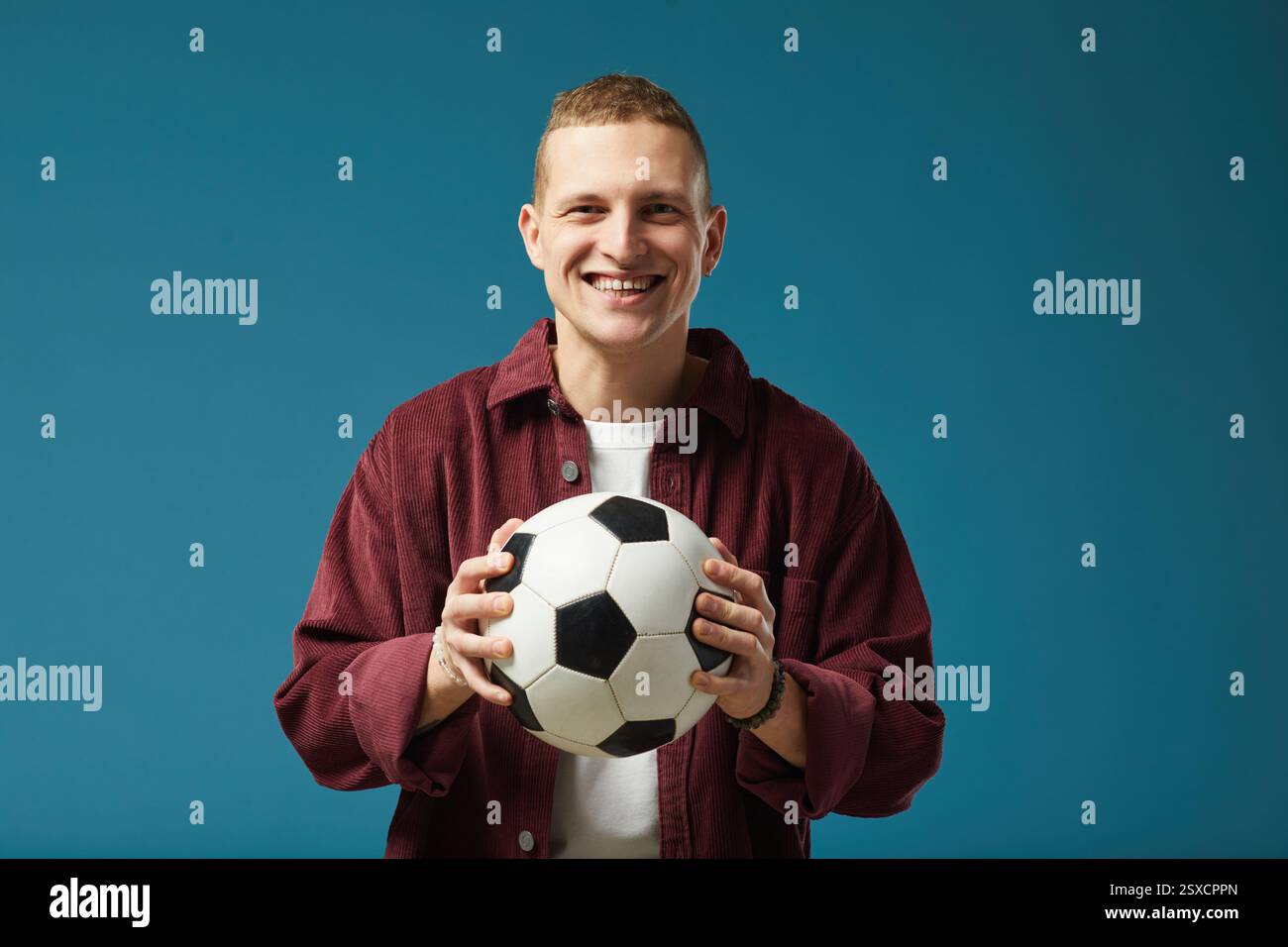 Lächelnder Junger Mann, Der Fußball Vor Blauem Hintergrund Hält Stockfoto