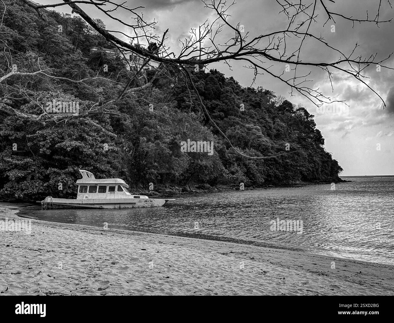 Makroschale auf warmem Sand mit Wellen und Booten im Hintergrund Eine schwarz-weiße Landschaft, in der ein Schiffbrüchiges Boot am Strand liegt Stockfoto