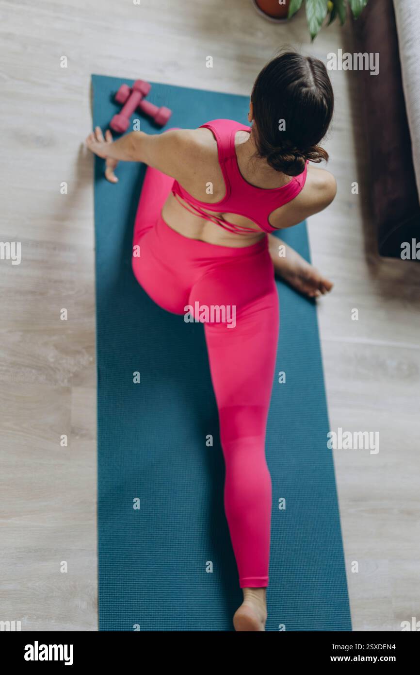 Frau in einem rosa Sportoutfit übt Yoga, dehnt sich zu Hause aus, von oben. Hochwertige Fotos Stockfoto