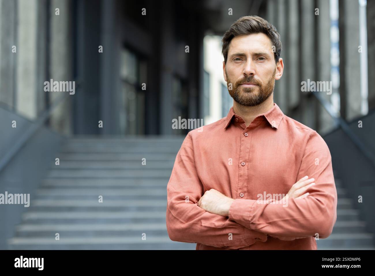 Porträt eines ernsthaften selbstbewussten Geschäftsmannes vor einem Bürogebäude, Mann mit überkreuzten Armen, der selbstbewusst in die Kamera blickt Stockfoto