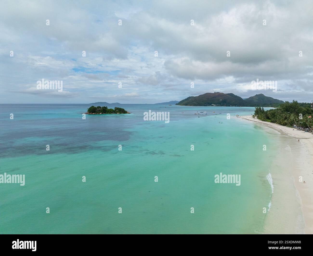 Blick aus der Vogelperspektive auf türkisfarbenes Wasser, das auf eine weiße Sandküste trifft, mit einer kleinen Insel in der Ferne. Anse Volbert Beach. Praslin, Seychellen. Stockfoto