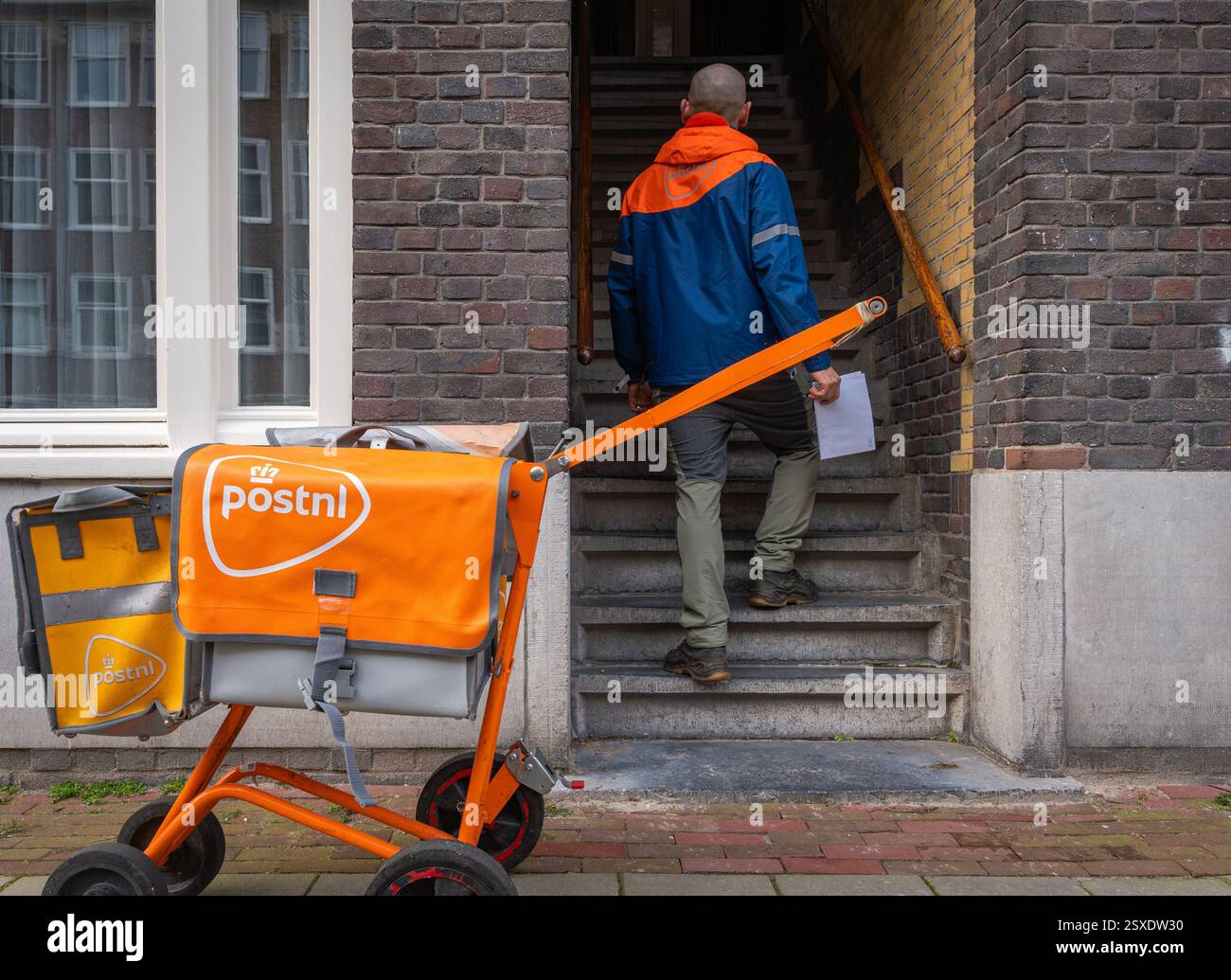 Amsterdam, Niederlande, 21.02.2025, PostNL-Mitarbeiter liefert Post, niederländischer Postbote mit Zustellwagen bei der Arbeit Stockfoto
