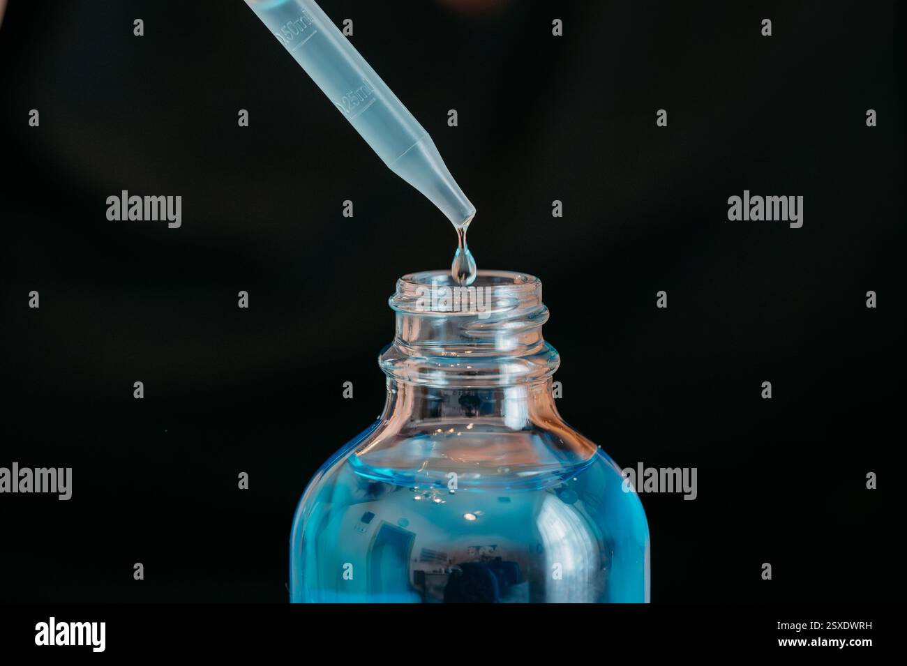 Nahaufnahme eines Tropfens, der blaues Serum in eine Glasflasche abgibt Stockfoto