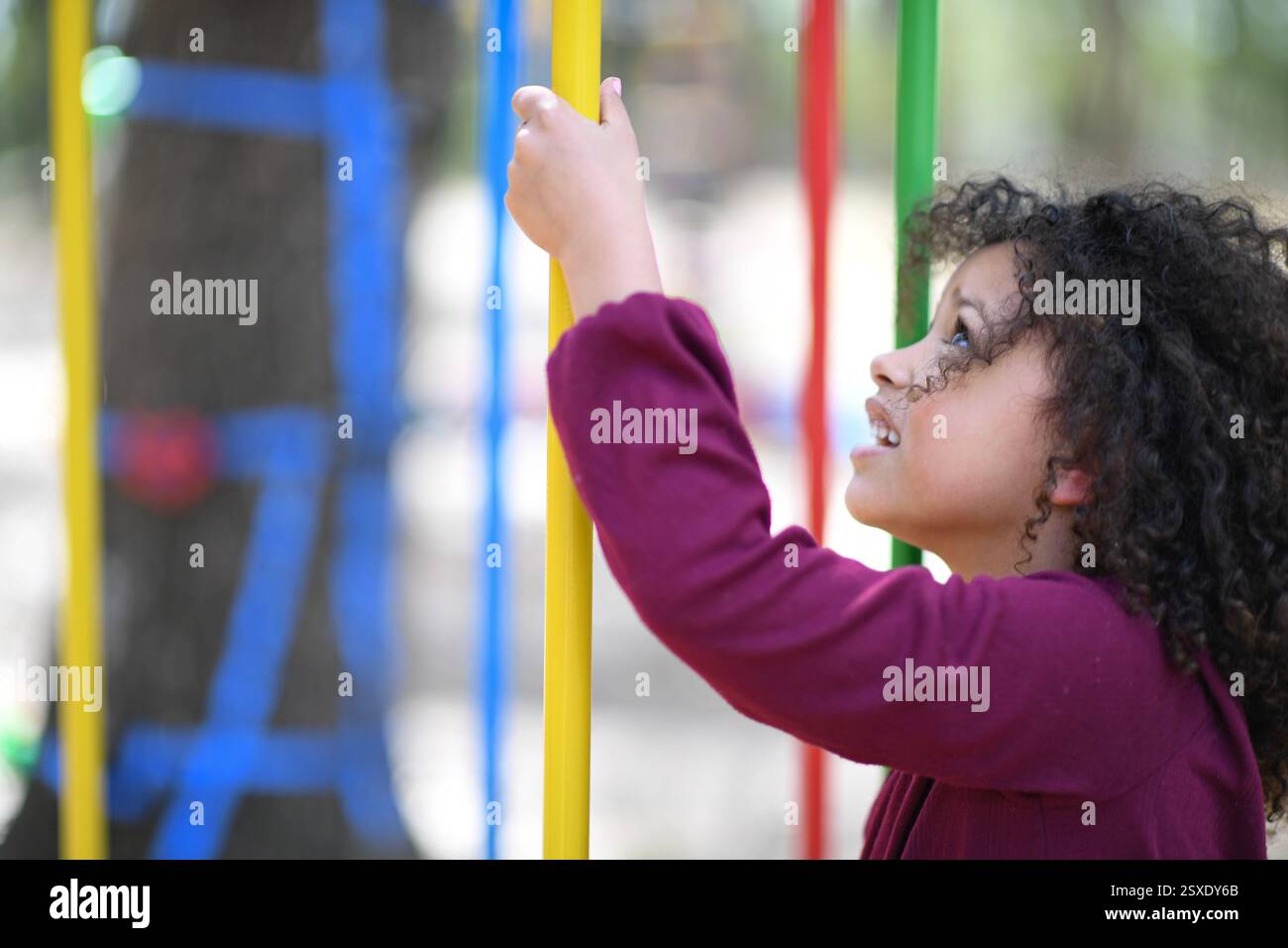 Lächelndes Mädchen, das bunte Spielplatzbars packt und aufgeregt aufblickt Stockfoto