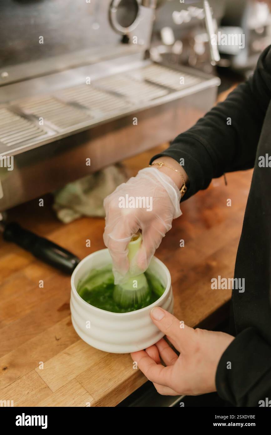 Barista rührt im Coffee Shop leuchtend grünen Matcha in einer Keramikschale Stockfoto