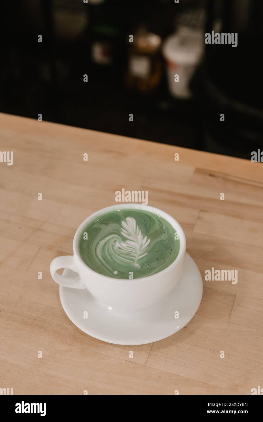 Matcha Latte mit Blatt Latte Art in weißer Tasse auf hölzernem Kaffeekocher. Stockfoto