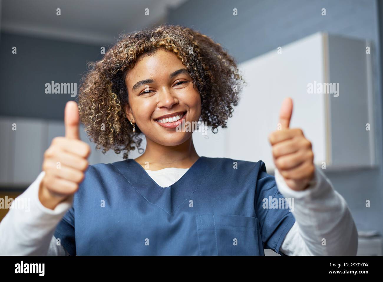 Lächelnder medizinischer Fachmann, der Daumen oben in heller Krankenhausumgebung gibt Stockfoto