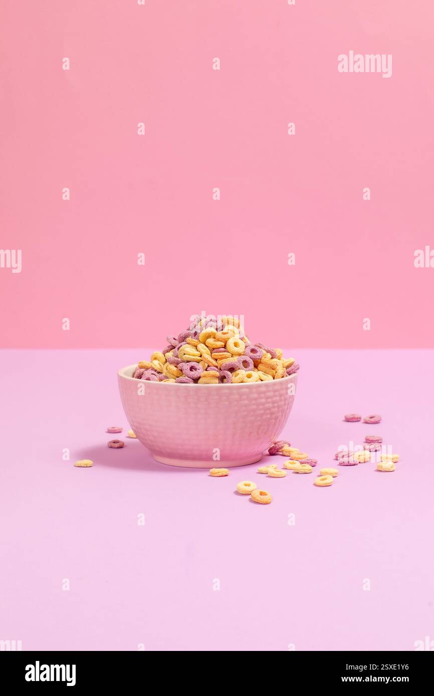 Eine Schüssel voller farbenfroher Fruchtschleifen auf pastellrosa Hintergrund. Helles, lustiges und nostalgisches Frühstück in minimalistischer Ästhetik. Stockfoto