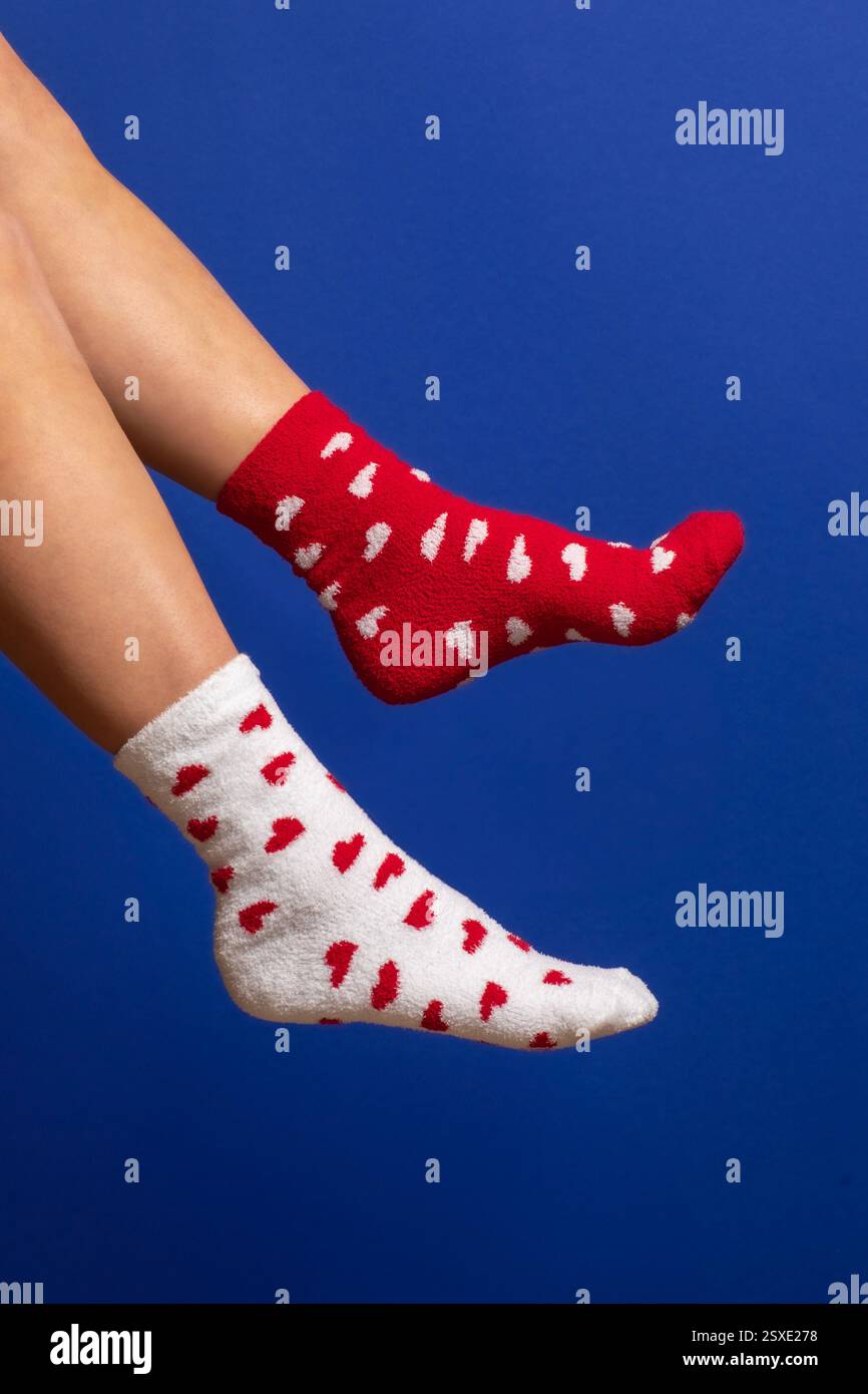 Bequeme, nicht passende Socken mit Herzmuster in Rot und weiß vor einem auffälligen blauen Hintergrund. Perfekt für Valentinstag oder gemütliche Winterstimmung. Stockfoto