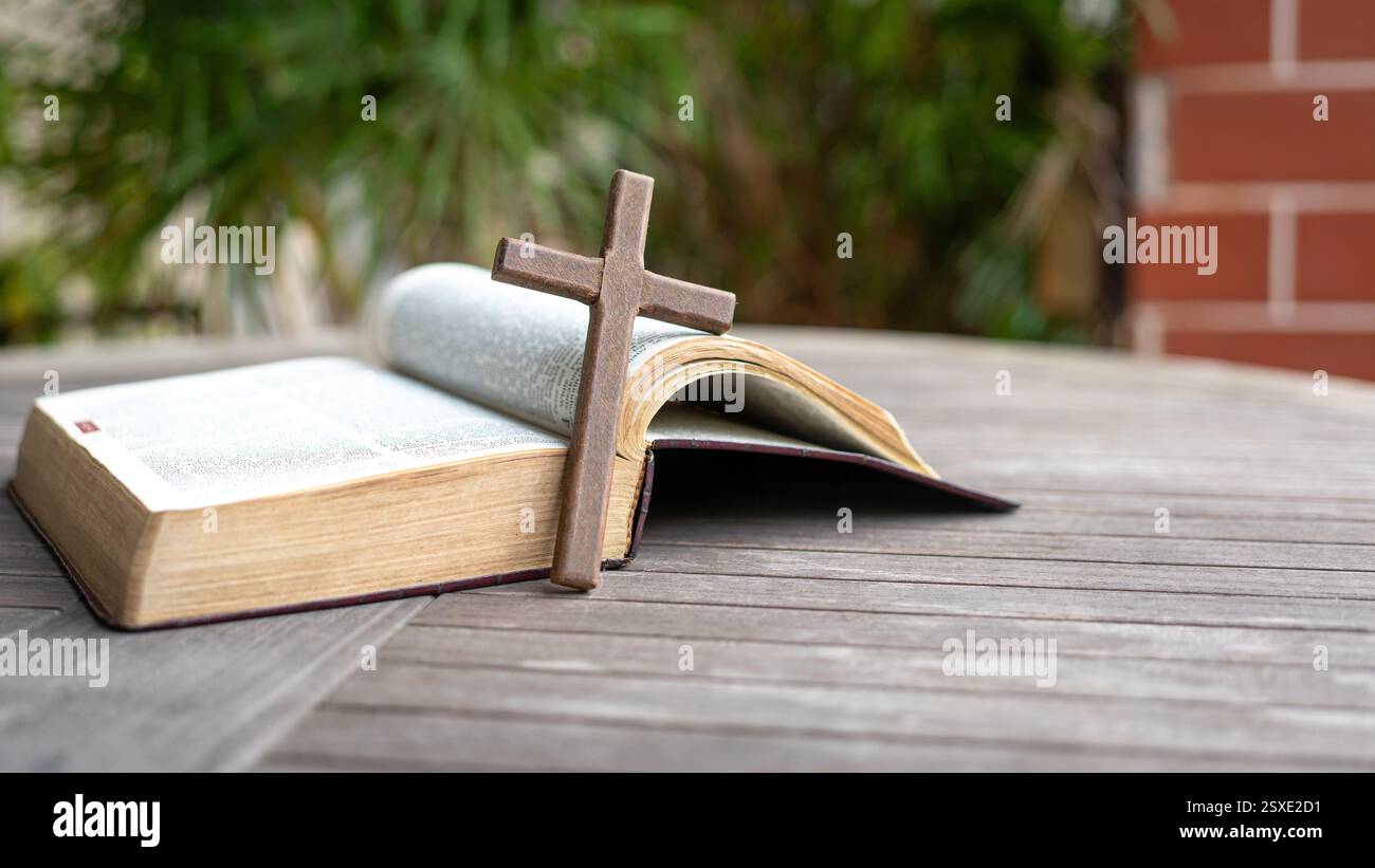 Hölzernes Kruzifix-Kreuz neben der Bibel. Auf dem Holztisch. Kopierbereich. Stockfoto