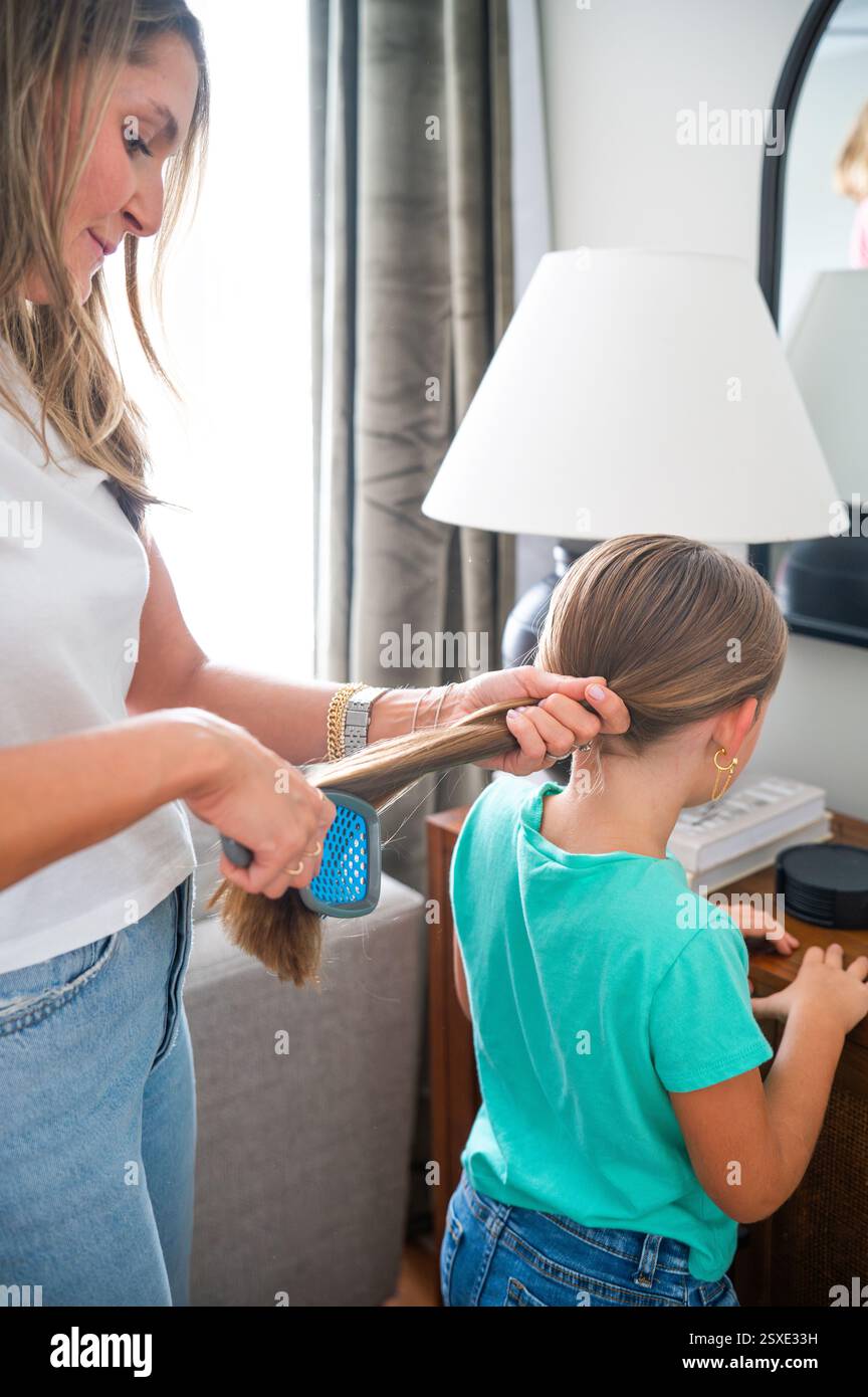 Mom putzt die blonden Haare der jungen Tochter zu Hause Stockfoto