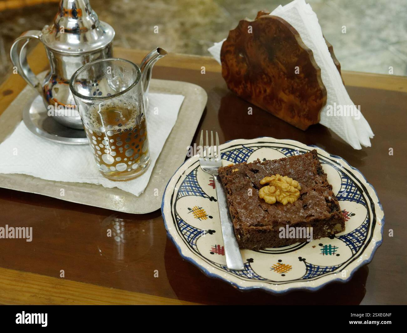 Schokoladenbrownie mit Walnuss und traditionellem Tee mit Teekanne, serviert auf einem Tisch in einem Café in der Stadt Essaouira, Marokko, Februar 2025 Stockfoto
