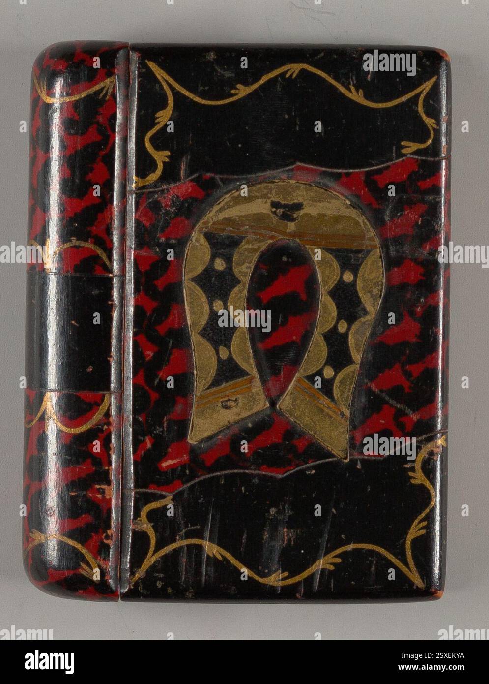 Glücksschachtel mit Schublade in Buchform (1800-1999) aus Lindenholz, rot lackiert mit goldenem und schwarzem Hufeisen-Design. Er verfügt über kurvenförmige Muster, goldene Kanten und eine Schublade, die mit einem mittleren schwarzen Band geöffnet werden kann. Stockfoto