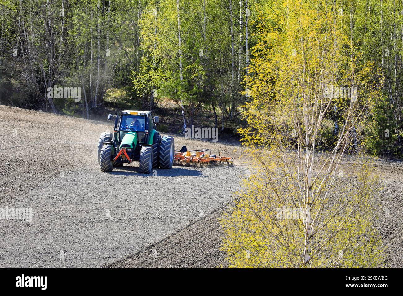 Feldbearbeitung mit Deutz-Fahr Agrotron-Traktor und Egge im Frühjahr. Landwirtschaftliche Landschaft mit Frühlingsbäumen. Salo, Finnland. Mai 2024. Stockfoto