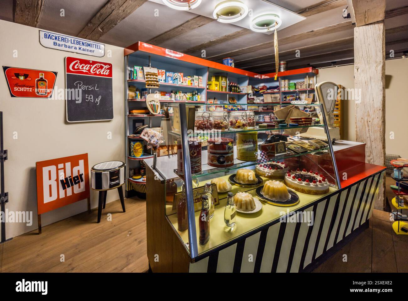 Rekonstruierter Eckladen in Deutschland. In einem deutschen Vintage-Supermarkt werden zum Verkauf stehende Artikel, darunter Kuchen, Süßigkeiten und Haushaltswaren, sowie eine Waage und ein Schild für Barbara Kainer gezeigt. Persil Reinigungsmittel kostet 59 Pfennig. Sattlertorstraße, Forchheim, Bayern, Deutschland Stockfoto