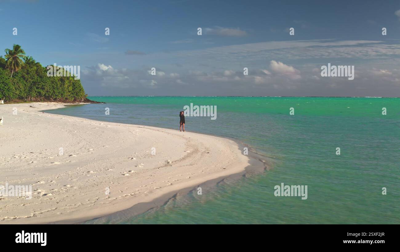 Bei einem gemütlichen Spaziergang entlang eines unberührten Strandes genießt eine junge Frau die Sonne und den atemberaubenden Blick auf maupiti türkisfarbenes Wasser Stockfoto