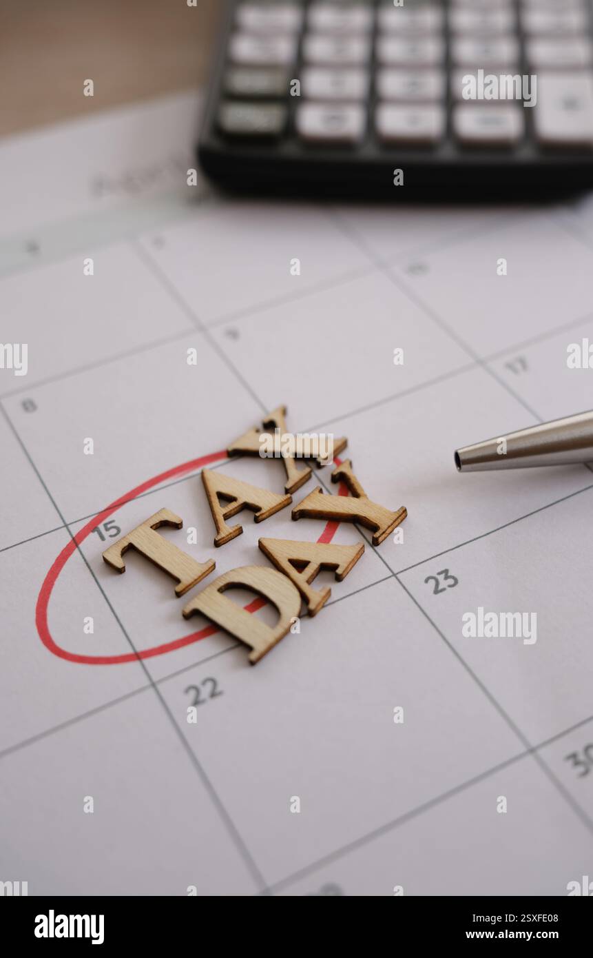 Vertikale Aufnahme der Erinnerung an den Steuertag auf einem Kalender mit Holzbuchstaben, Stift und Rechner Stockfoto