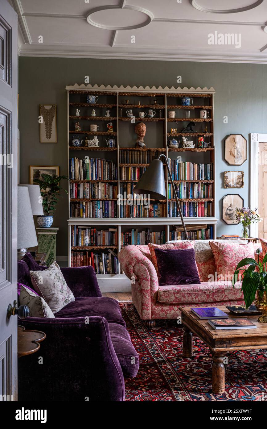 Vintage-Bücherregal mit Damastsofa Chesterfield und lila Samt mit orientalischem Teppich in Bayfield Hall, einem Landhaus aus dem 18. Jahrhundert in Norfolk, Großbritannien. Stockfoto