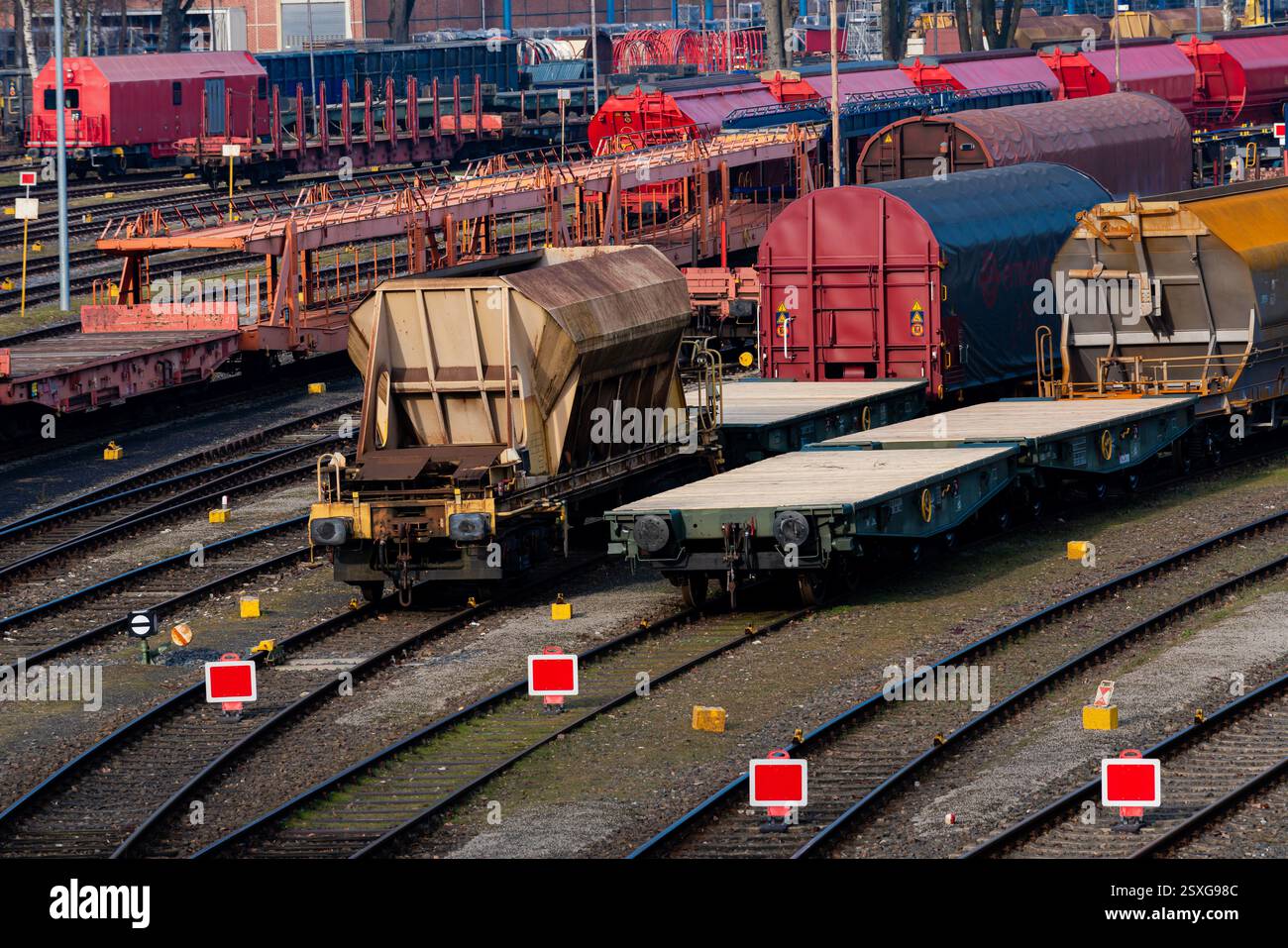 Auf einem belebten Bahnhofsgelände stehen verschiedene Güterwagen, die auf mehreren Gleisen unter klarem blauem Himmel geparkt sind. Leuchtend rote Markierungen und ein gut organisiertes Layout Stockfoto