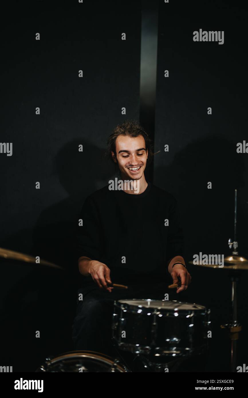 Junger Schlagzeuger, der bei einer Bandprobe in einem Musikstudio mit Begeisterung übt Stockfoto