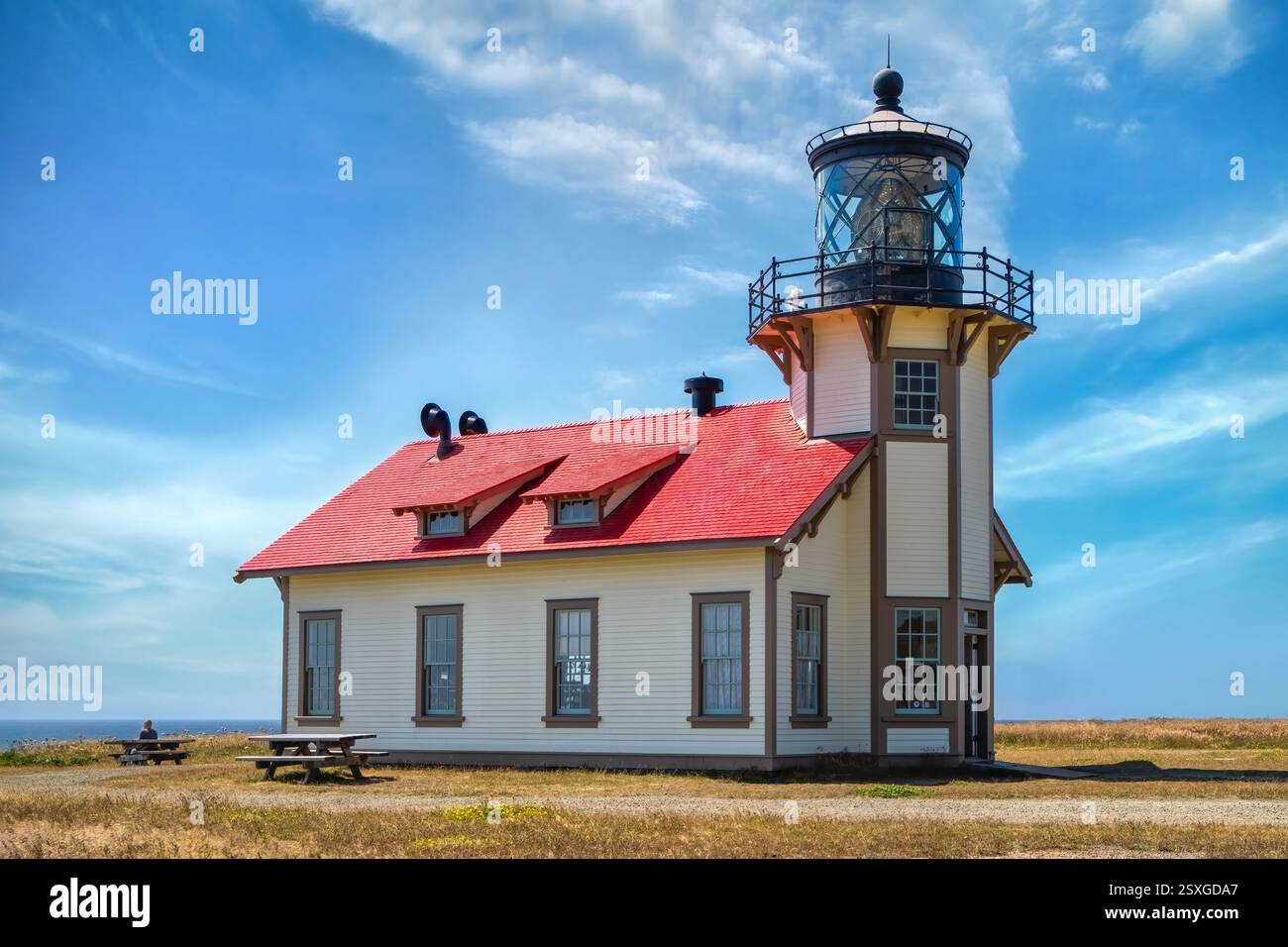 Ein bezaubernder Leuchtturm, bekannt als Point Cabrillo, mit einem hellroten Dach, steht auf einer grasbewachsenen Landschaft unter einem klaren blauen Himmel. Seine weiße Fassade und Umgebung Stockfoto