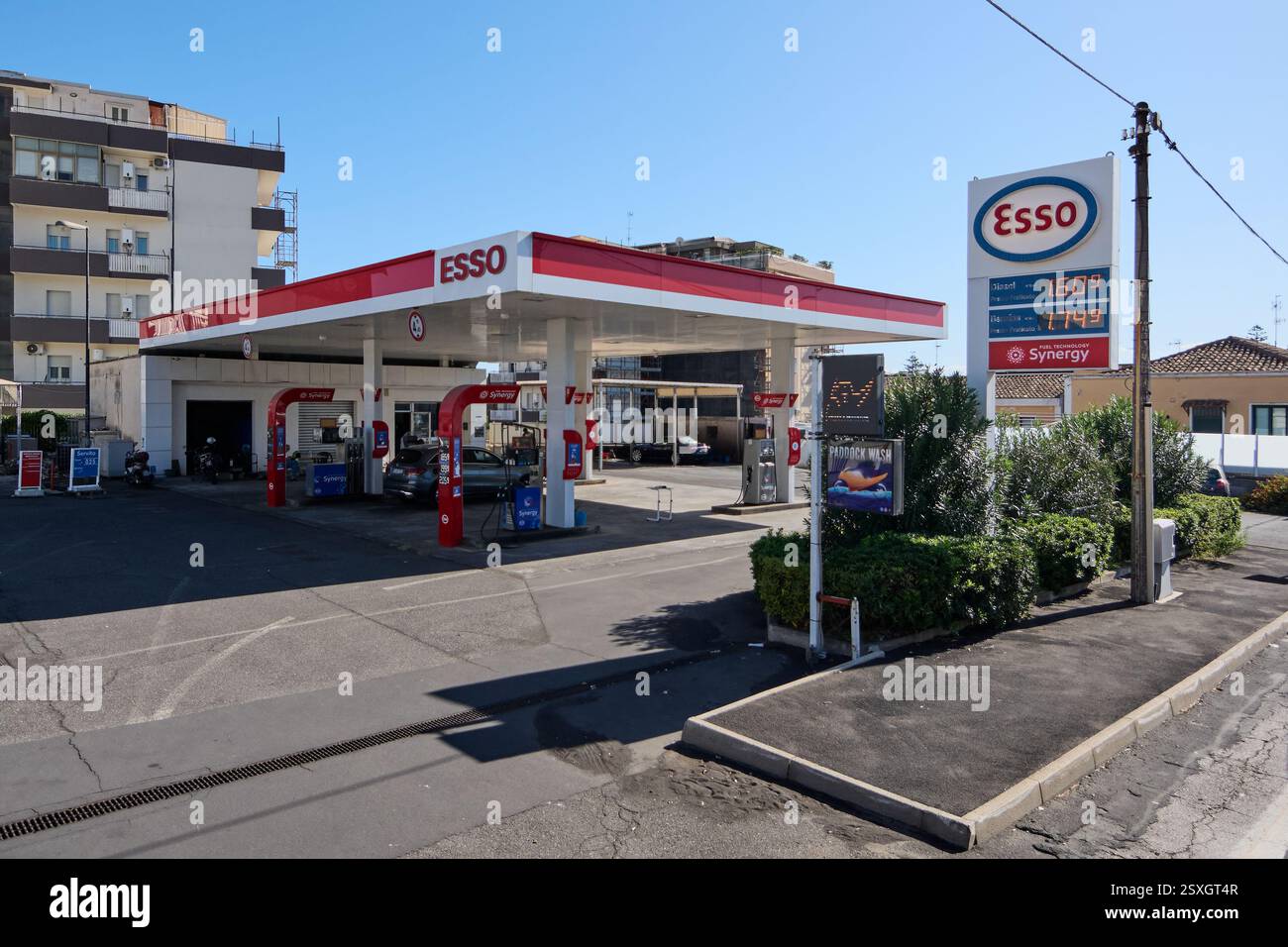 Catania. Italien - 24. Februar 2025: Moderne städtische Tankstelle. Eine Esso-Tankstelle vor einem mehrstöckigen Gebäude mit mehreren Fahrzeugen parkten aro Stockfoto