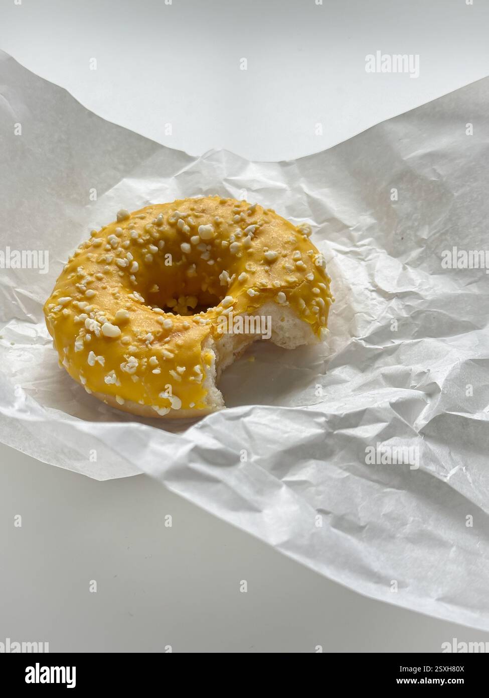Gebissener gelber Donut in weißem Papier auf weißem Tisch Stockfoto