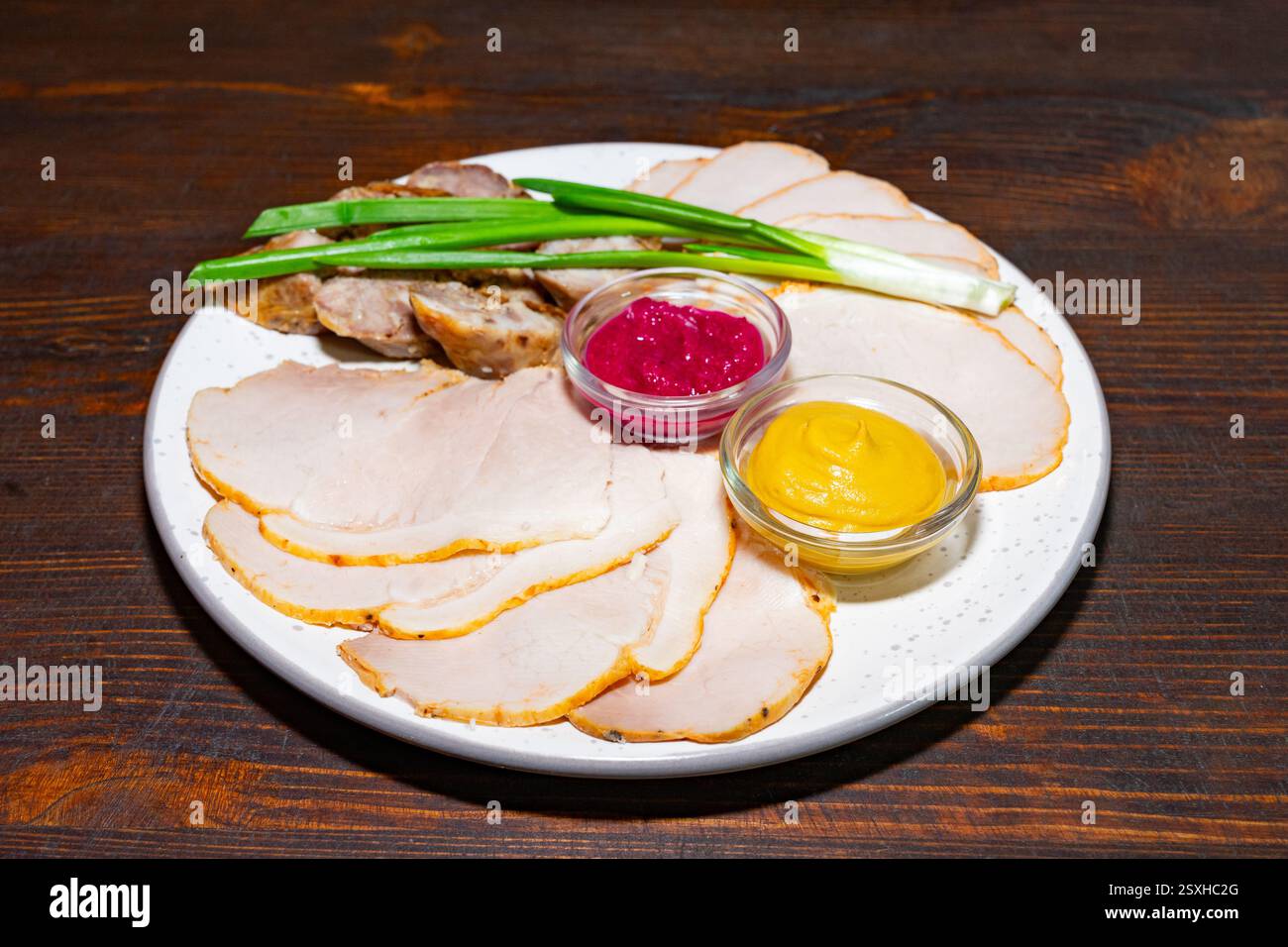 Eine Platte bietet dünn geschnittene Aufschnitte und rustikale Brotscheiben. Zwei kleine Schüsseln enthalten Senf und einen würzigen roten Dip, garniert mit frischem gr Stockfoto