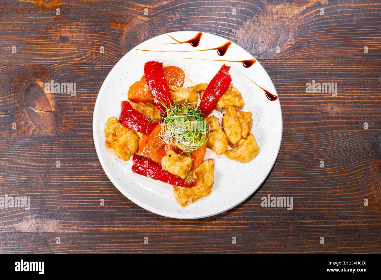 Ein lebhaftes Gericht mit knusprigen Hähnchenstücken kombiniert mit roter Paprika und frischem Gemüse. Die Präsentation beinhaltet einen Spritzer Soße und Grün Stockfoto