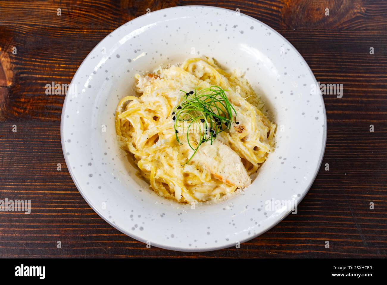Es wird eine Schüssel cremiger Fettuccine-Pasta serviert, garniert mit frischen Kräutern. Das Gericht besteht aus einer reichhaltigen Sauce und einem Streusel Käse, wobei ein Feinkost präsentiert wird Stockfoto