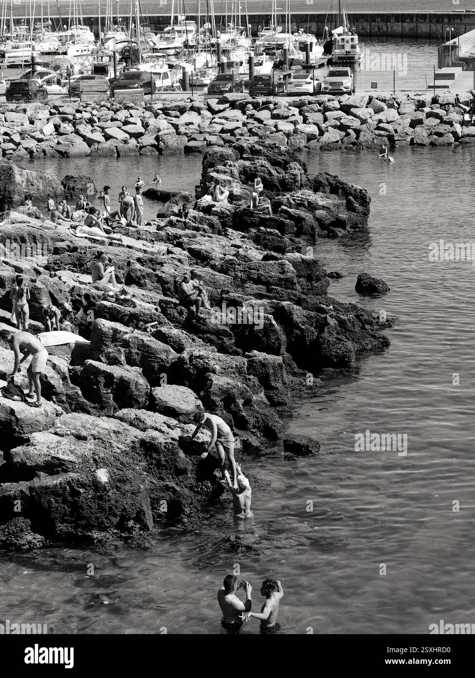 Sonnenanbeter und Schwimmer genießen die felsige Küste am Strand von Santa Marta mit Segelbooten im Hintergrund. Stockfoto