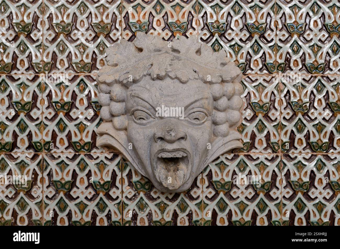 Aufwändig geschnitzter grotesker Steinbrunnenauslauf, der auf traditionellen portugiesischen Azulejo-Fliesen gesetzt ist Stockfoto