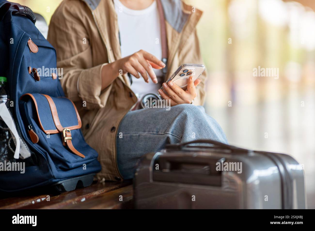 Eine Nahaufnahme des Mädchens, das das Telefon hält, während es auf einer Holzbank am Bahnhof oder Bahnhof sitzt. Stockfoto