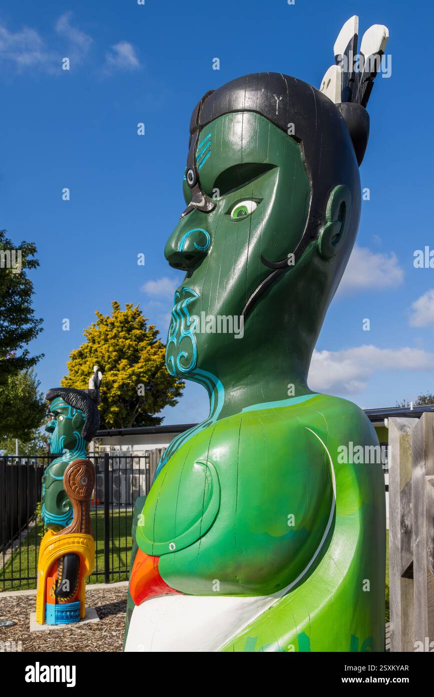 Hell gemalte Maori-Holzschnitzereien eines Mannes und einer Frau vor einer Schule in Tauranga, Neuseeland Stockfoto