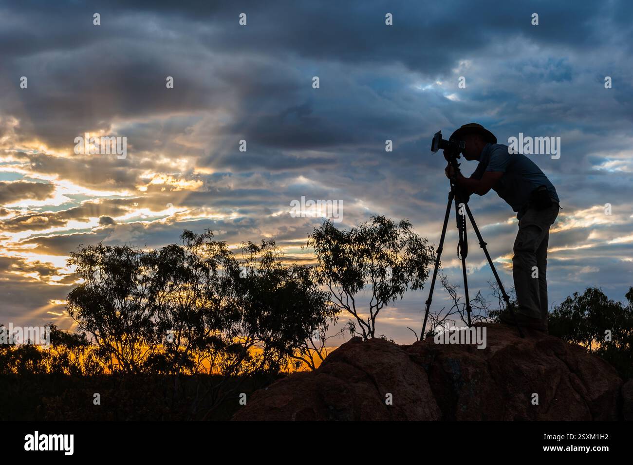 Ein Landschaftsfotograf mit Silhouetten komponiert seine Aufnahme auf einem Felsbrocken für eine Komposition bei Sonnenuntergang im Undarra in Queensland, Australien. Stockfoto