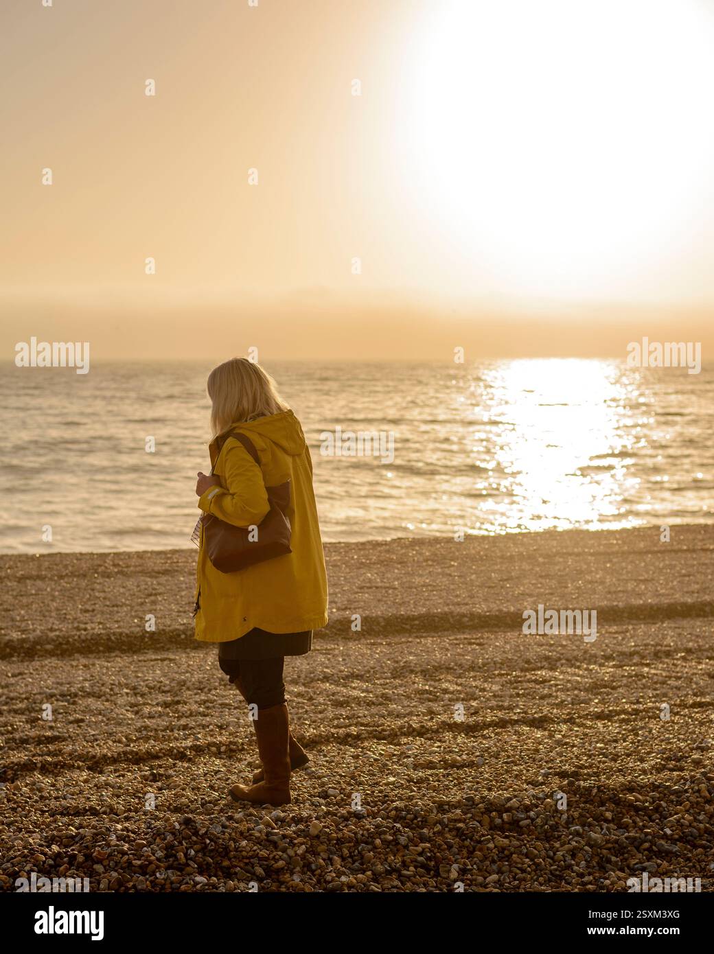 Frau, die an steinigen Strand im Winter Sonne mit hellem Sonnenlicht auf dem Meer dahinter läuft. Stockfoto