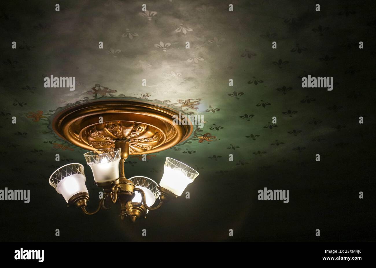 Ein wunderschön gefertigter Kronleuchter mit Glasschirmen wirft warmes Licht in einem elegant dekorierten Vintage-Raum mit einem kunstvollen Deckendesign in der Abenddämmerung. Stockfoto Ein wunderschön gefertigter Kronleuchter mit Glasschirmen wirft warmes Licht in einem elegant dekorierten Vintage-Raum mit einem kunstvollen Deckendesign in der Abenddämmerung. Stockfoto