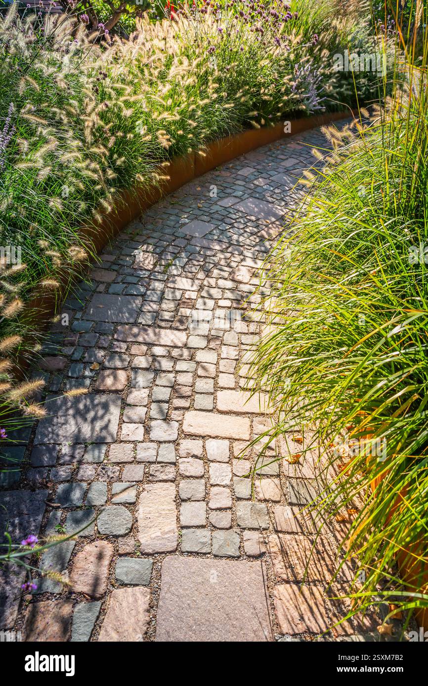 Detail des Gartenweges mit Steinplatten mit Rindenmulch und einheimischen Pflanzen. Landschaftsbau- und Gartenkonzept. Stockfoto