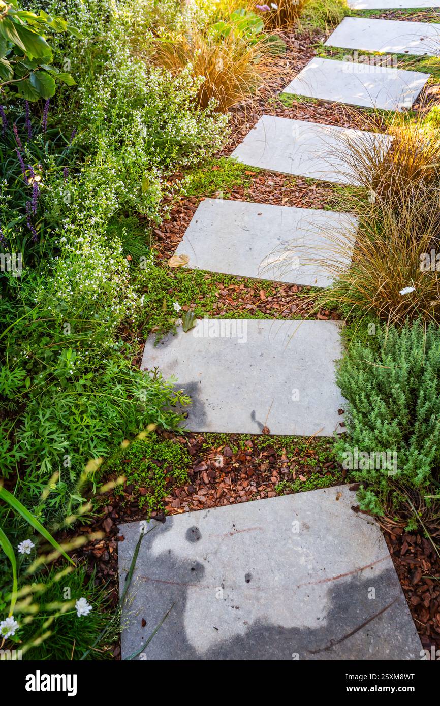 Detail des Gartenweges mit Steinplatten mit Rindenmulch und einheimischen Pflanzen. Landschaftsbau- und Gartenkonzept. Stockfoto