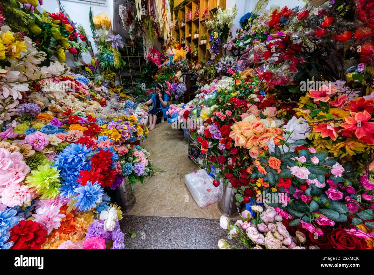 In einem Blumenladen im historischen Zentrum von Hanoi werden bunte Blumen zum Verkauf angeboten. Die Verkäuferinnen telefonieren mit ihrem Handy. Stockfoto