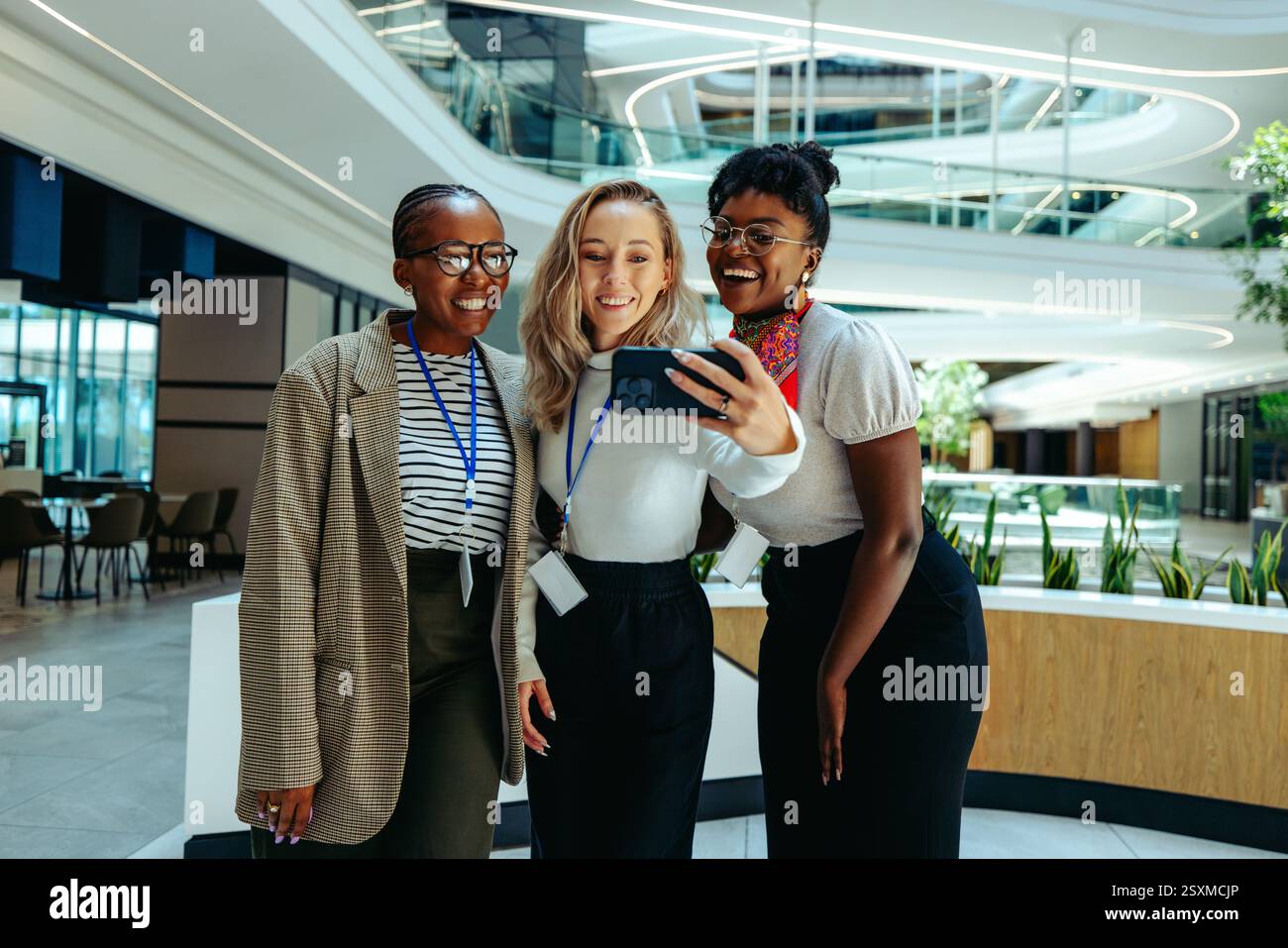 Eine Gruppe von freundlichen Kollegen lächelt, während sie gemeinsam ein Selfie in einer modernen Unternehmensumgebung machen und dabei Teamarbeit und Kameradschaft hervorheben. Stockfoto