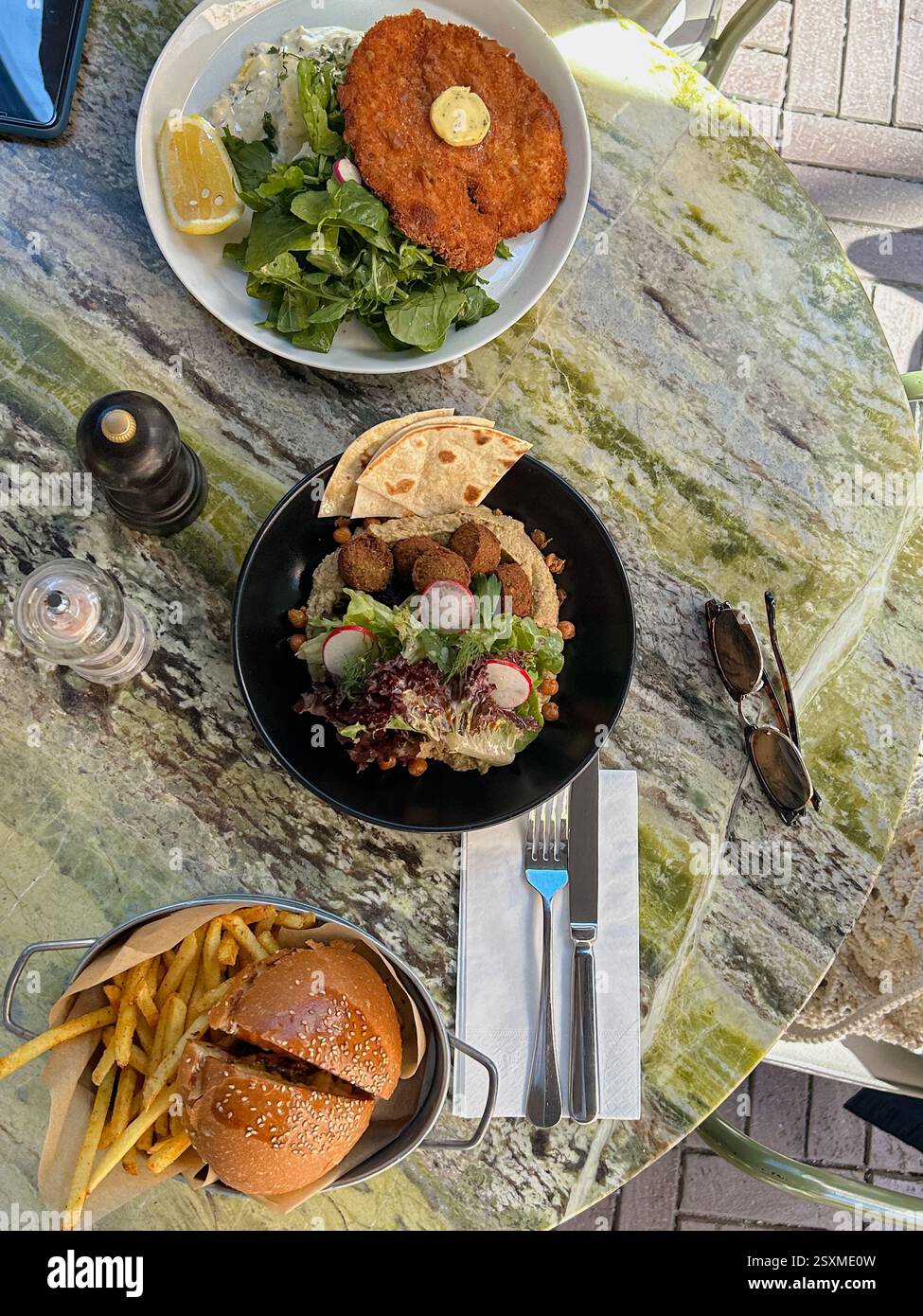 Dieses Bild zeigt ein wunderschön eingerichtetes Abendessen im Freien mit drei verschiedenen Gerichten auf einem grünen Marmortisch. Die obere Platte ist mit einem Golden-br Stockfoto