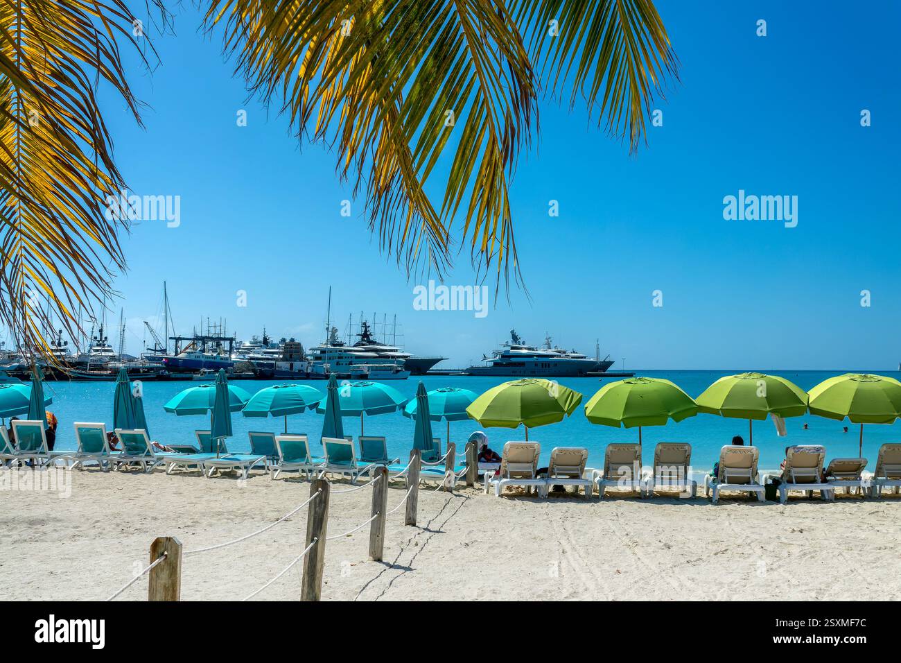 Stühle und Sonnenschirme am Great Bay Beach mit Booten im Yachthafen von Philipsburg, karibische Landschaft, Insel St. Maarten (St. Martin), niederländische Westindien Stockfoto