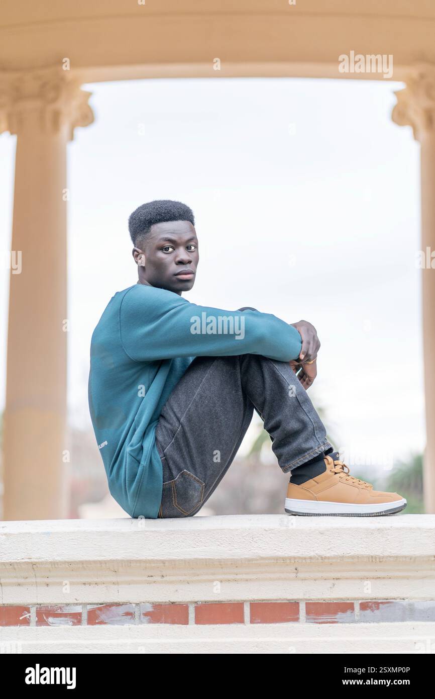 Nachdenklicher junger Mann sitzt auf einer niedrigen Mauer im Balboa Park, San Diego, Kalifornien Stockfoto