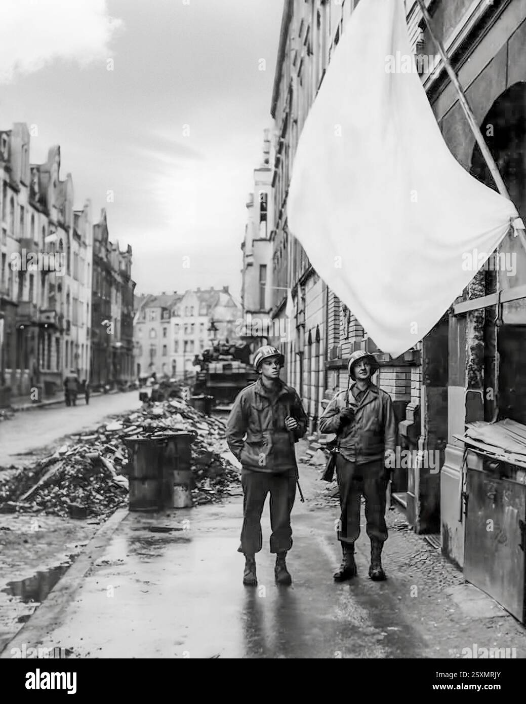 Zwei US-Abgeordnete mit weißer Flagge nach der Schlacht von Köln, Teil der Operation Lumberjack, dem Vormarsch der Alliierten, der vom 5. Bis 7. März 1945 stattfand und zur Eroberung der Stadt führte. Die alliierten Kolonnen näherten sich Köln aus drei Richtungen, wobei die 3. Panzerdivision aus Nordwesten, die 104. Infanteriedivision aus Westen und die 9. Panzerdivision südlich der Stadt zusammen mit der 9. Infanteriedivision aufbrachen. Am 5. März startete die 3. Panzerdivision einen letzten Vormarsch auf Köln. Am 6. März zogen die amerikanischen Kolonnen ins Stadtzentrum. Stockfoto