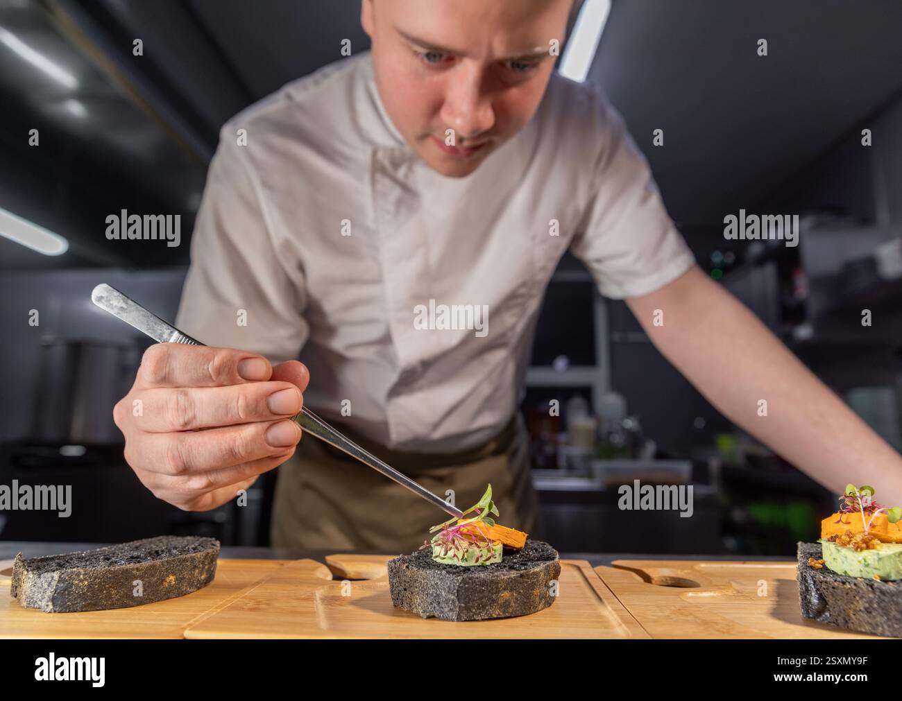 Küchenchef legt in der Restaurantküche Microgreens auf Gourmet-Häppchen mit Pinzette Stockfoto