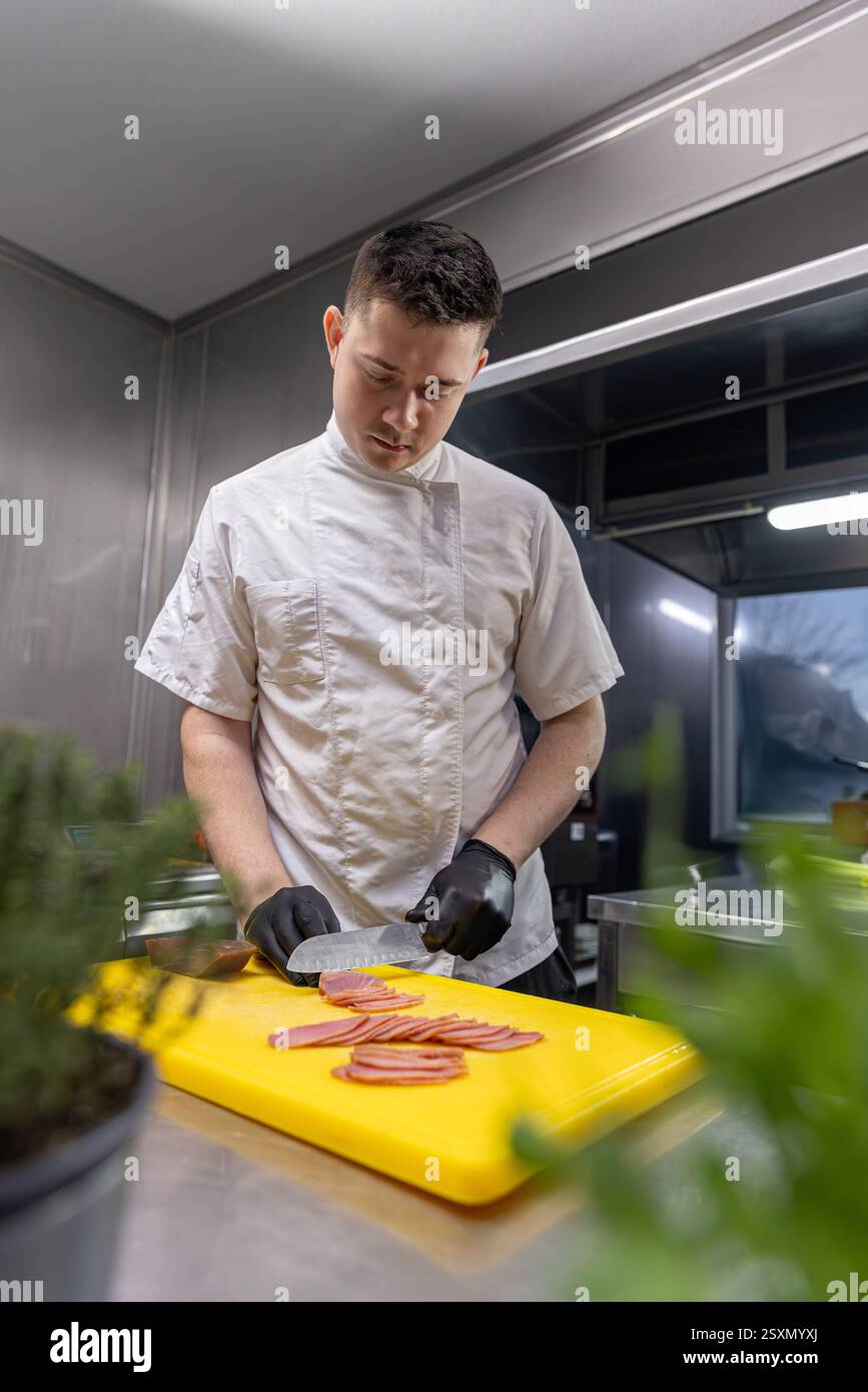 Junger Koch schneidet frischen Thunfisch auf einem gelben Schneidebrett und bereitet eine köstliche Mahlzeit in einer professionellen Küche zu Stockfoto